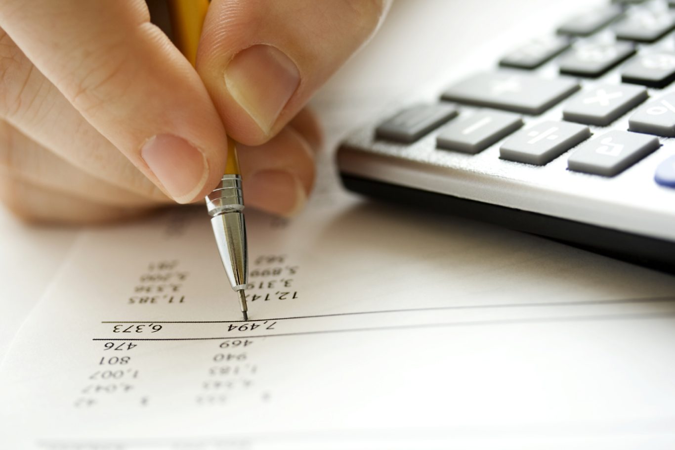 Main dans une position d'écriture, avec un stylo sur une feuille près d'une calculatrice.