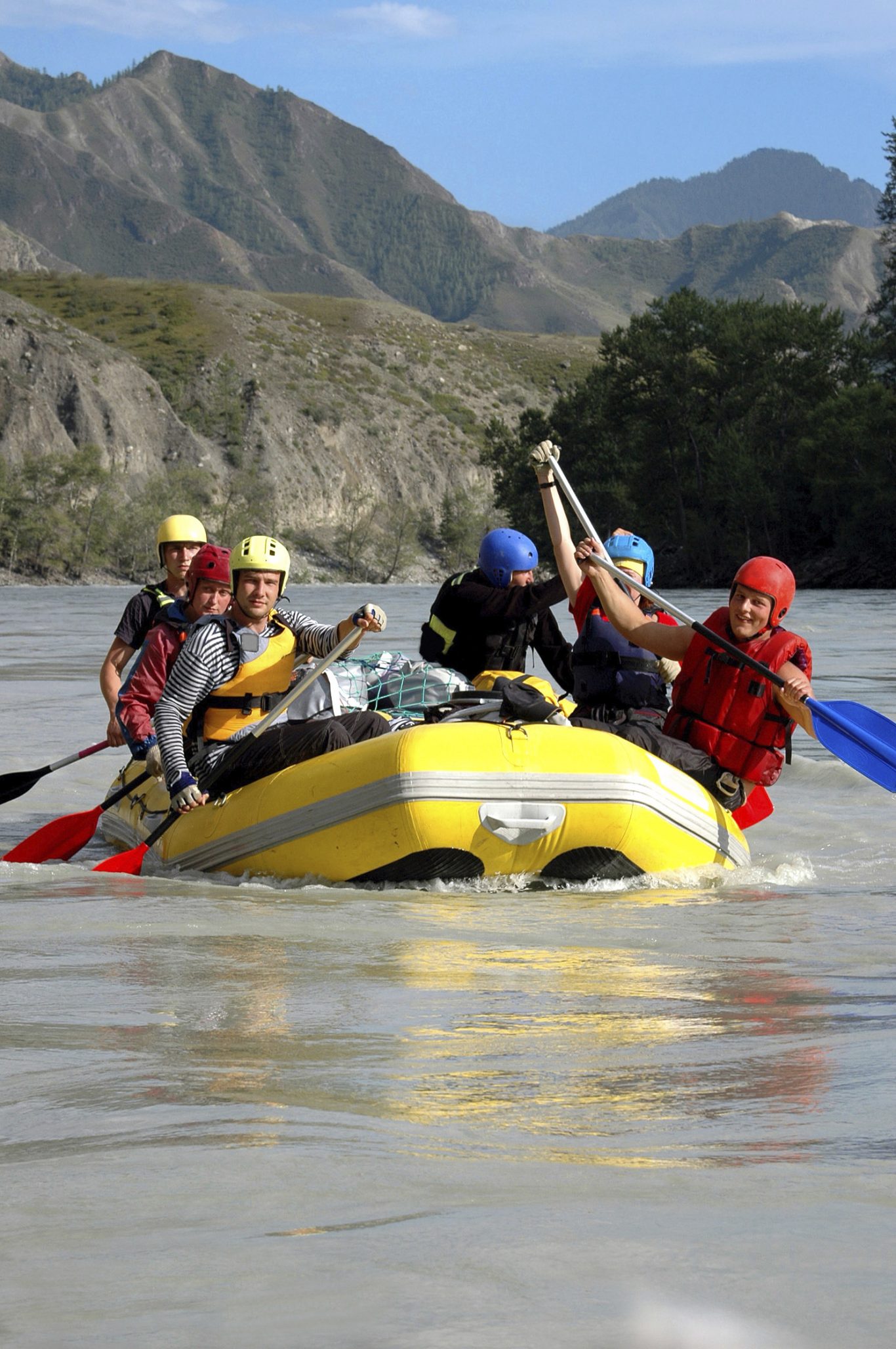 Groupe de personnes en rafting sur une rivière entourée de montagnes.