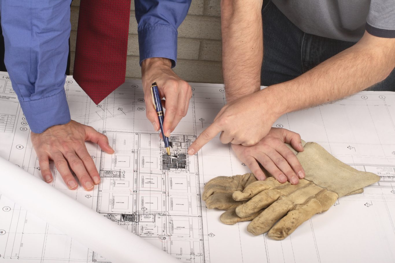 Deux personnes examinant des plans de construction, gants de travail à proximité.