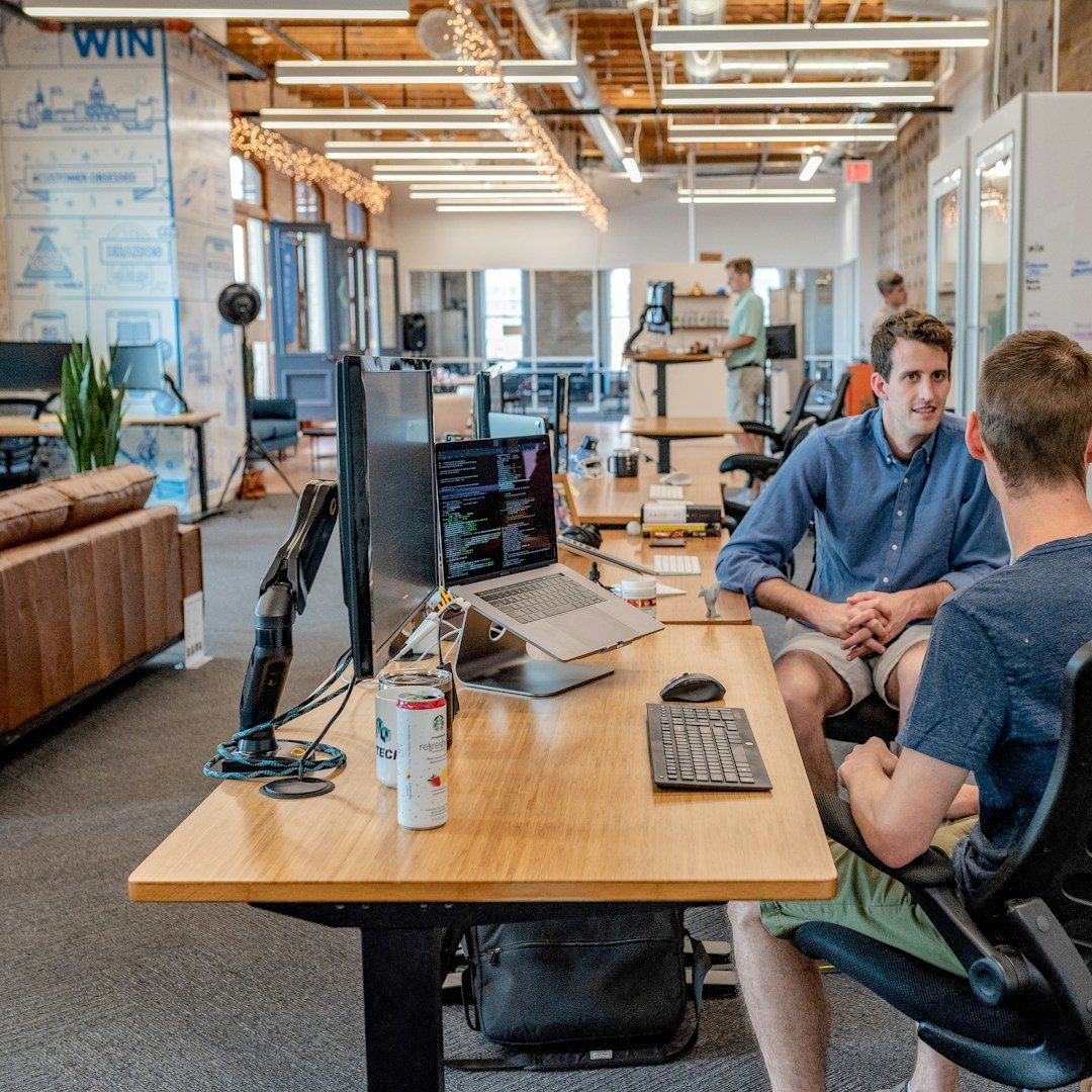 Deux personnes discutent dans un bureau moderne avec des équipements informatiques.