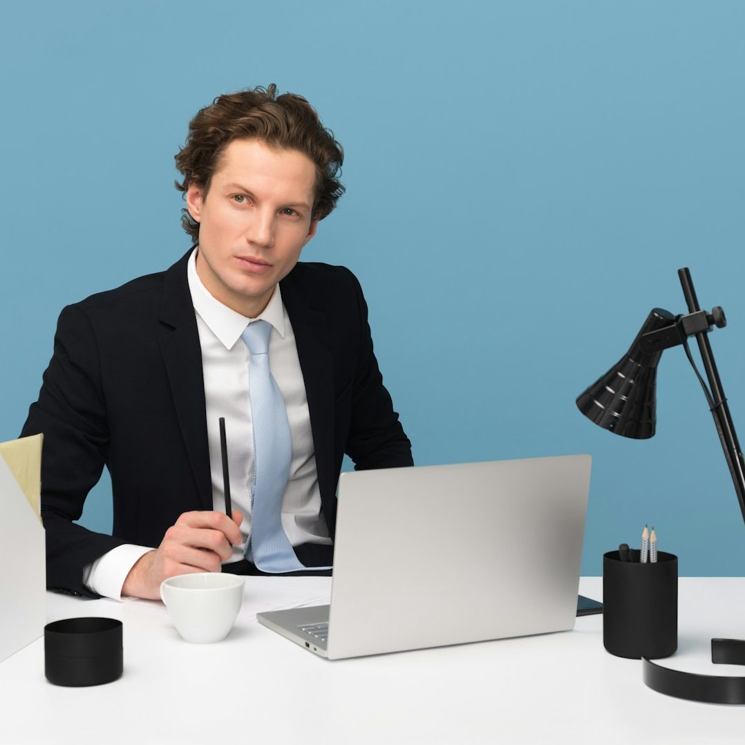 Homme en costume assis à un bureau moderne, regardant l'objectif avec un ordinateur portable.