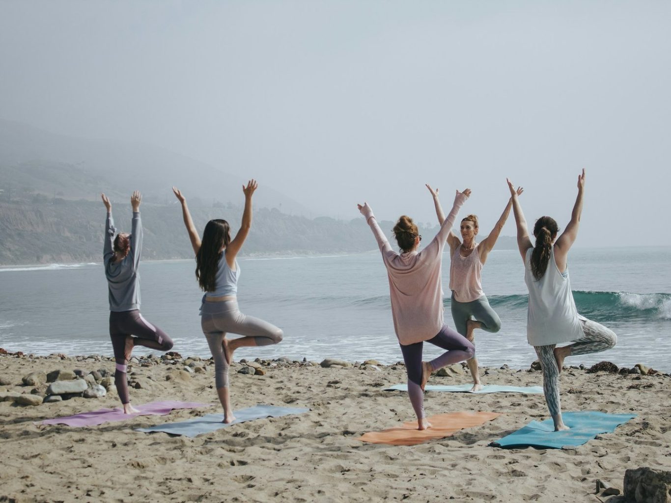 Groupe de personnes pratiquant le yoga sur la plage, avec la mer en arrière-plan.
